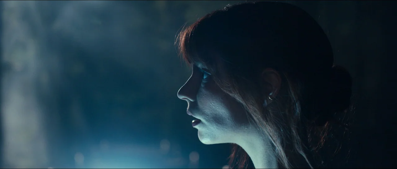 The Menu (2022) movie still: closeup — A woman is framed in side profile against a dark, blurry nighttime environment. Soft blue light hits the side…