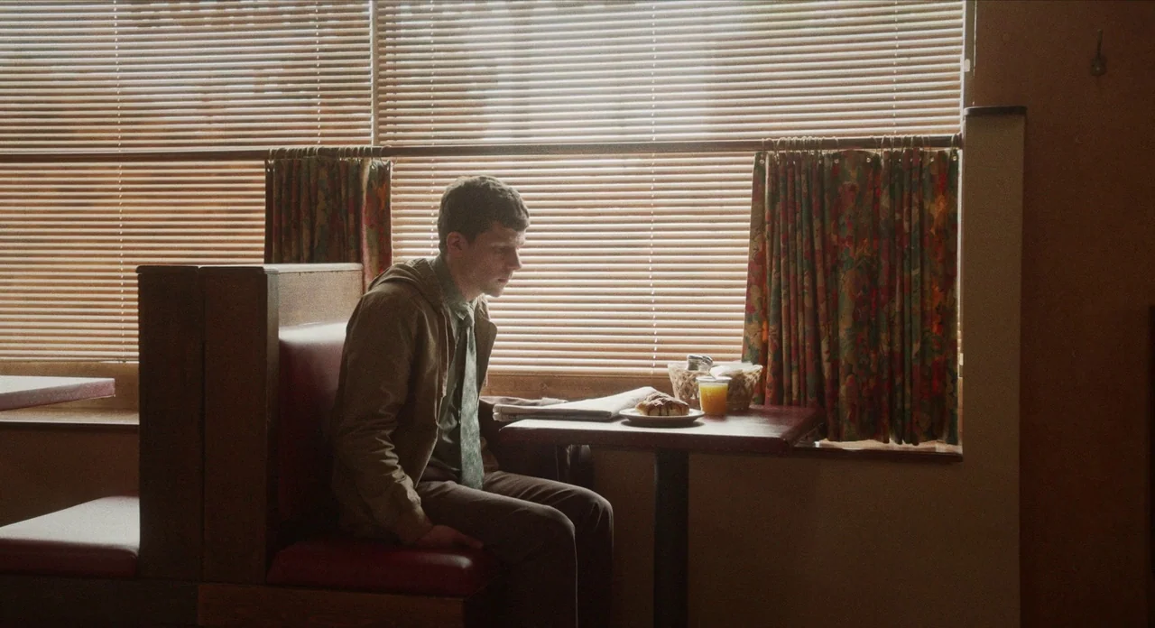 The Art of Self Defence (2019) movie still: medium — A diner booth features red vinyl seating and horizontal blinds covering the window behind. A…