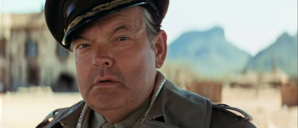Catch 22 (1970) movie still: closeup — A man in a military uniform stands in a dry, sunlit desert village. He looks forward with a steady gaze…