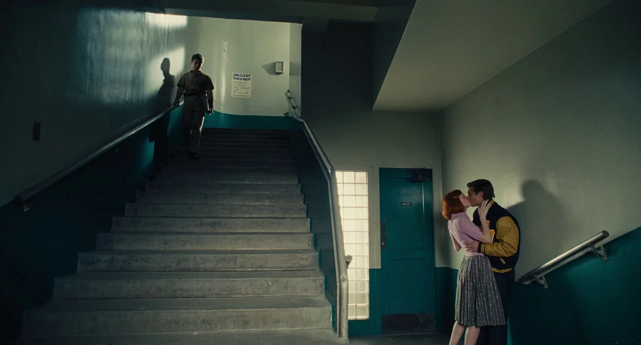 The Fabelmans (2022) movie still: wide — A concrete staircase in a mid-century school building has teal wainscoting and glass blocks. A couple…
