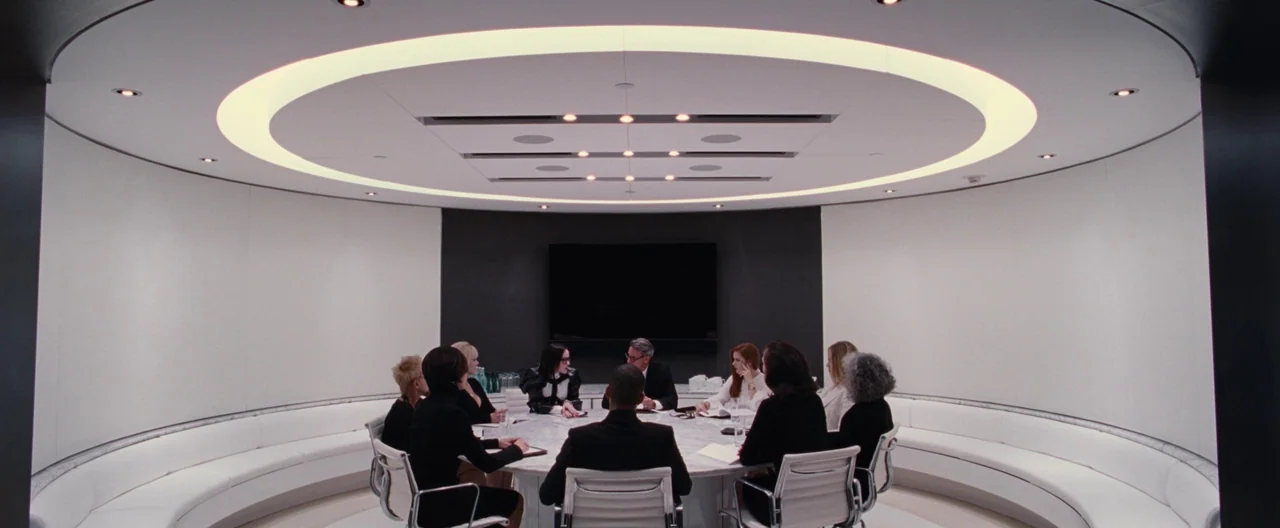Nocturnal Animals (2016) movie still: wide — A circular, minimalist white conference room features a marble table and curved seating. A group of…