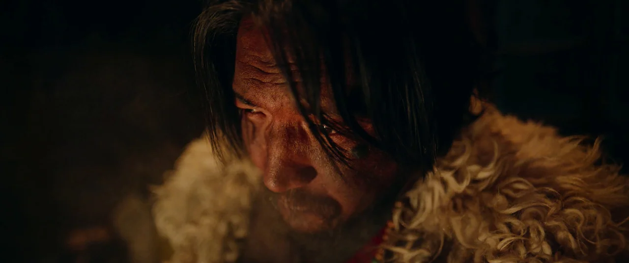 One And Four (2021) movie still: closeup — A dark, unidentifiable outdoor space illuminated by a warm, nearby fire source. A man with a dirt-smeared…