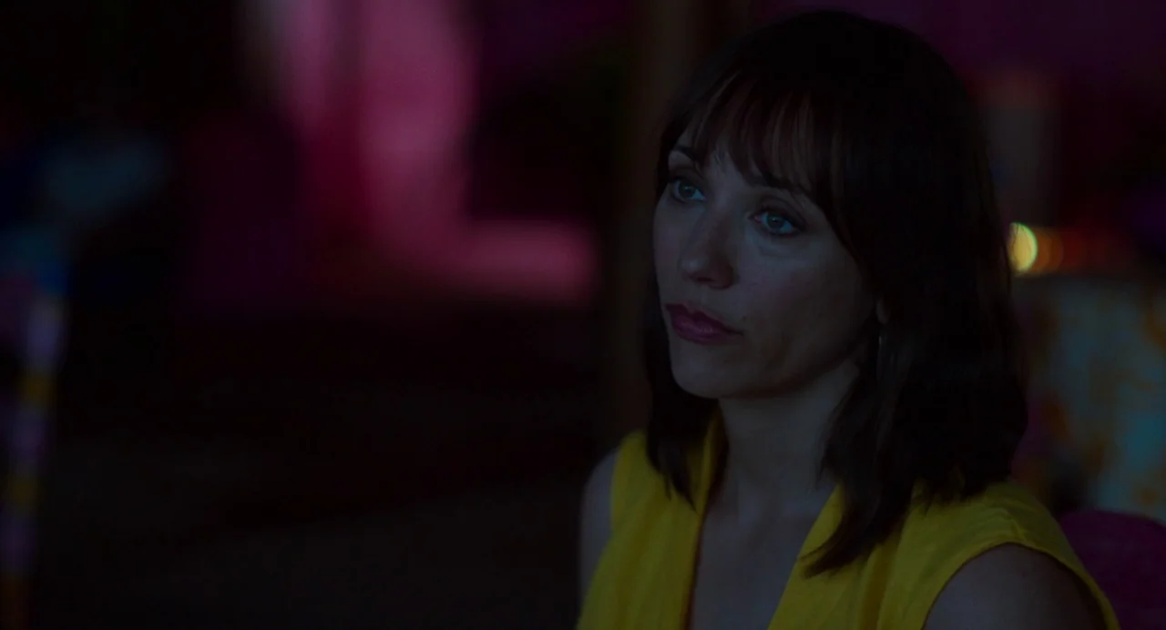 On The Rocks (2020) movie still: closeup — A dimly lit room is bathed in saturated pink and purple light shadows. A woman with dark hair wears a…