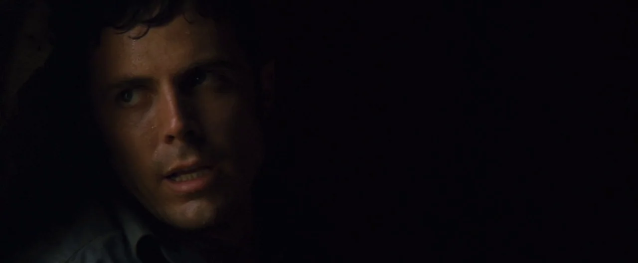 Ain’t Them Bodies Saints (2013) movie still: closeup — A dark, undefined interior space is cast mostly in deep shadow. A man with wet, dark hair is…