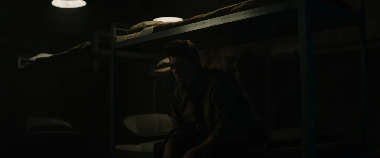 Mudbound (2017) movie still: medium — A dark military barracks room filled with metal bunk beds in a row. A young soldier sits alone on the bottom…