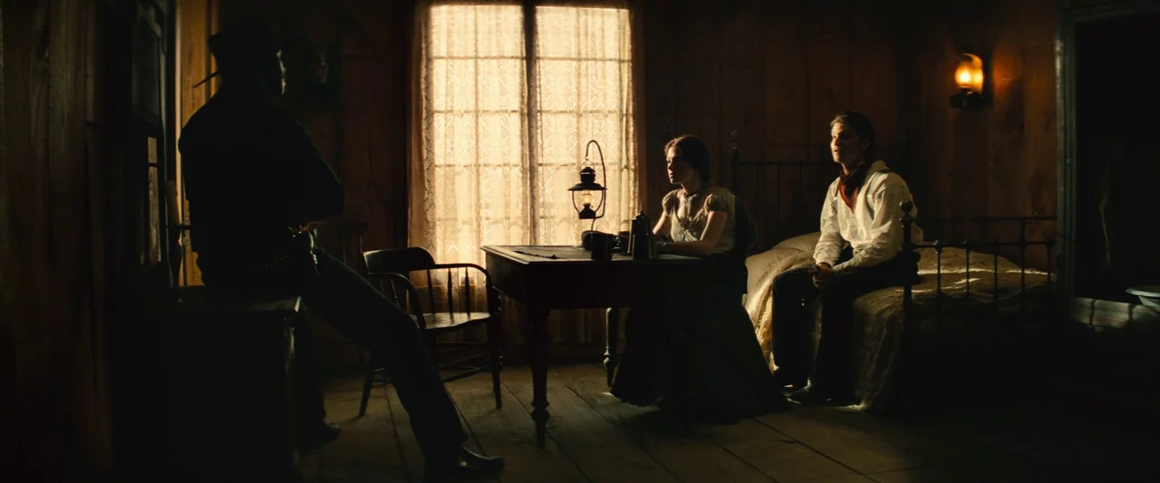 The Magnificent Seven (2016) (2016) movie still: wide — A rustic wooden cabin features horizontal wall planks and a large central window. Three…