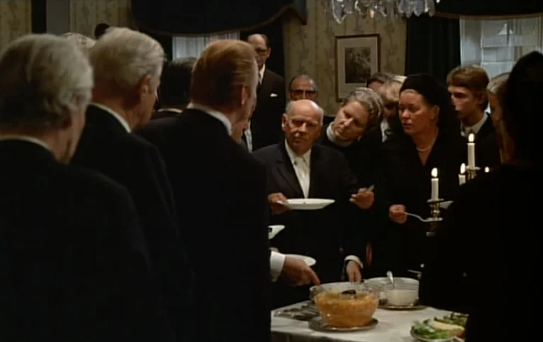 Giliap (1975) movie still: medium — A group of formally dressed people gather around a table laden with food. The room features traditional decor,…