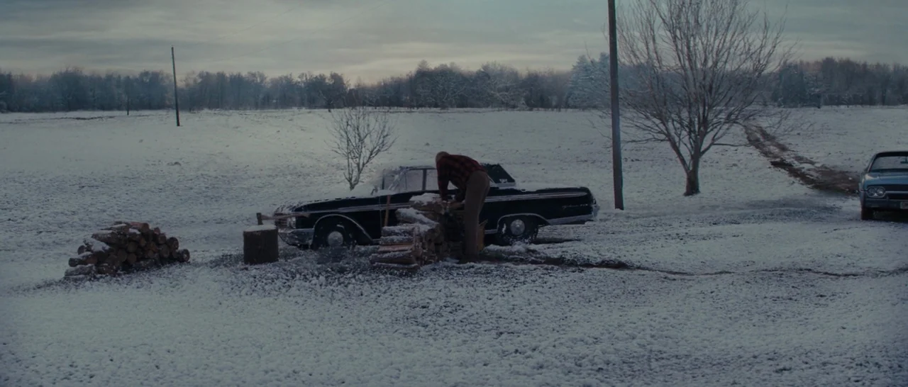 Loving (2016) movie still: wide — A snow-covered rural field features a black vintage car and a stack of wood. An older man dressed in a flannel…