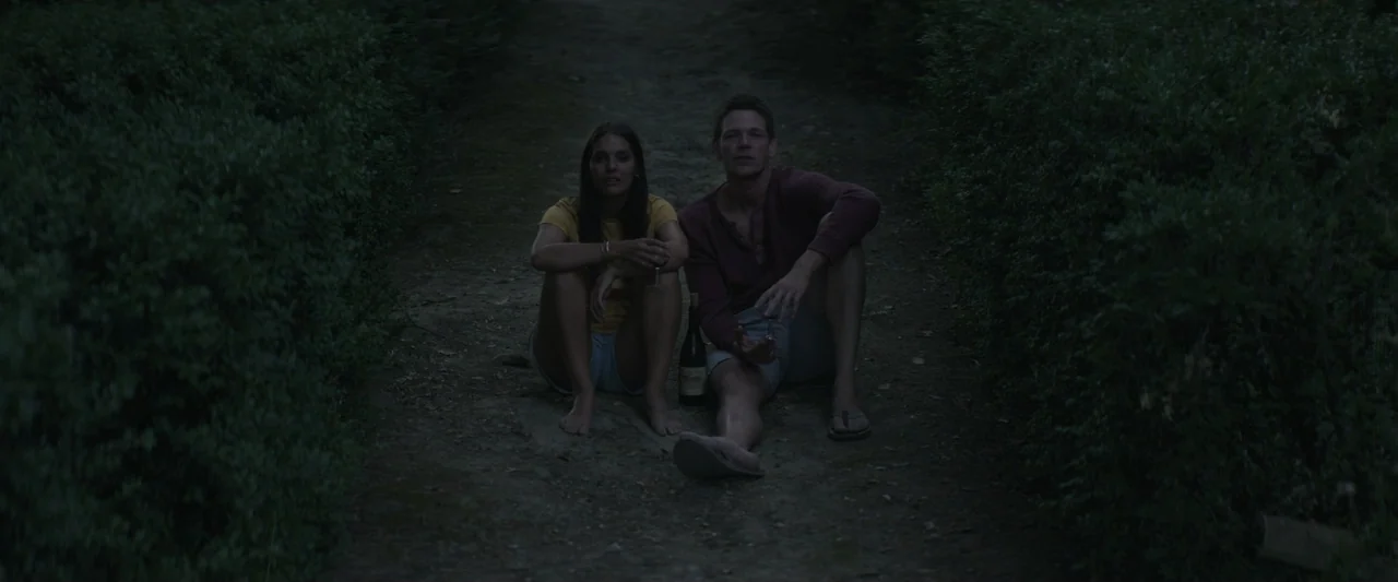 The Only One (2021) movie still: medium — A man and a woman sit on a dirt path bordered by dense green hedges. The two subjects are sitting on the…