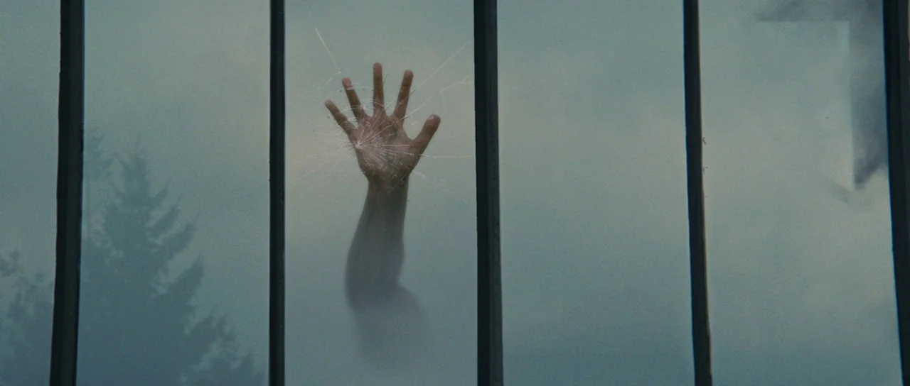 The Incredible Hulk (2008) movie still: closeup — A translucent pane of glass featuring a central spiderweb crack sits in a frame. A human hand…