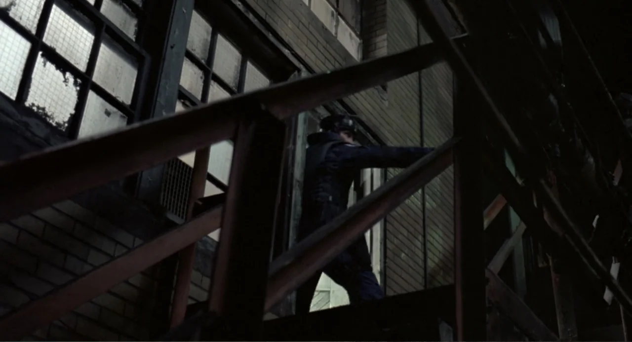 RoboCop (2014) movie still: medium — A dark, gritty industrial stairwell features metal railings and large brick-framed windows. A tactical officer…