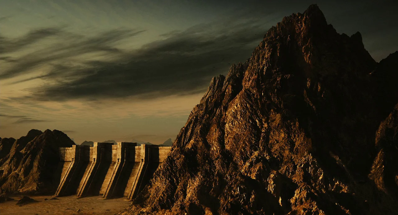 The Immortals (2011) movie still: establishing — A monolithic concrete dam spans a dry terrain between jagged, shadow-cast mountain cliffs. Dark,…