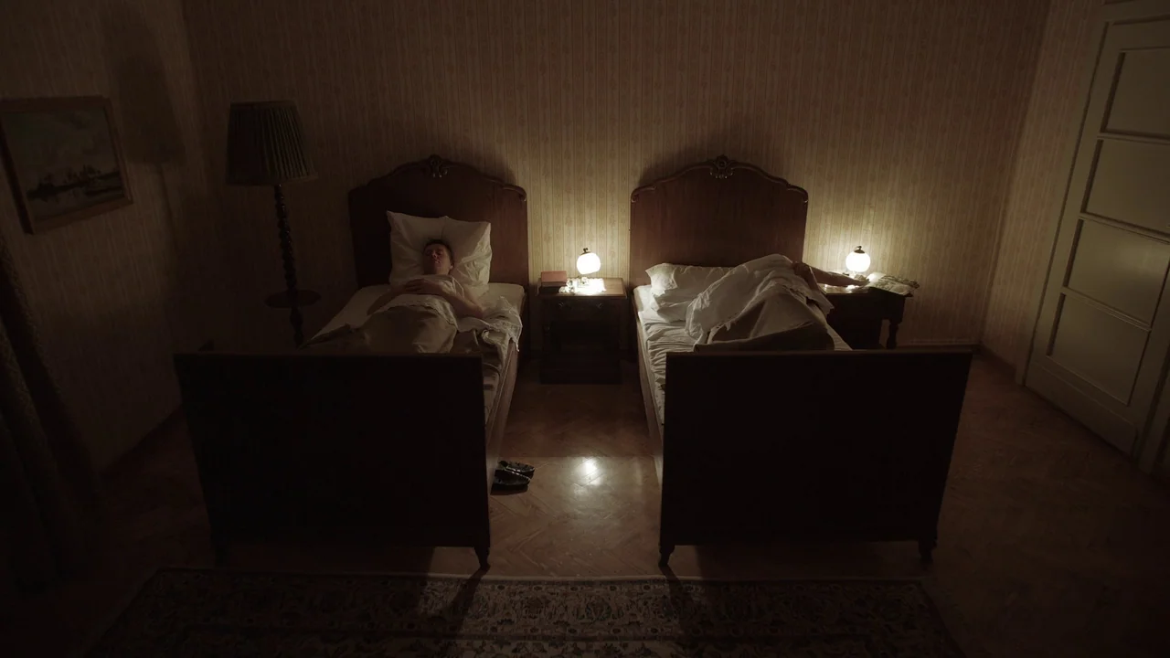 The Zone Of Interest (2023) movie still: wide — A dated interior space features two wooden twin beds placed symmetrically against a floral wall. A…