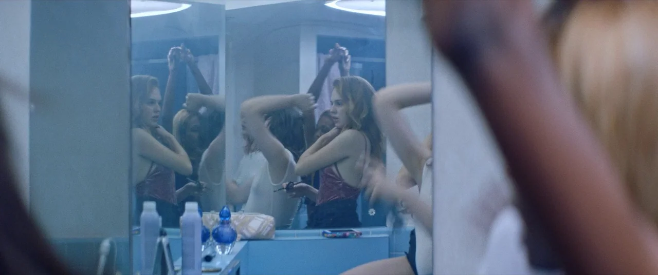Assassination Nation (2018) movie still: medium — A well-lit bathroom features blue-tiled surfaces and multiple reflective mirrors reflecting a…