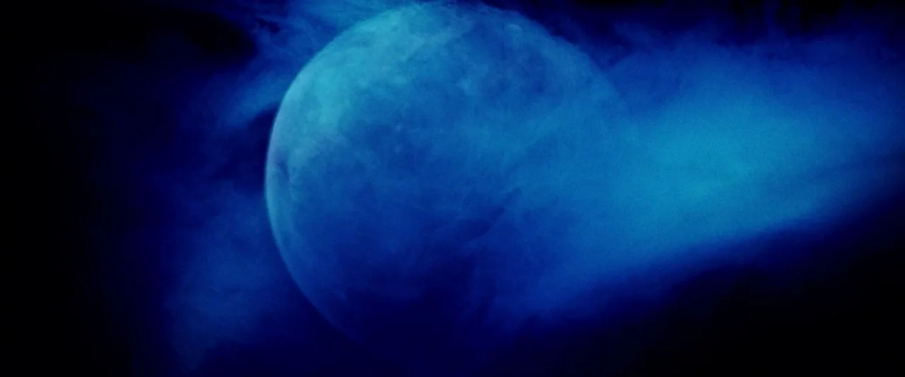 Moon Garden (2022) movie still: closeup — A planetary sphere sits suspended in the dark void of deep space. Dense blue interstellar gas billows…