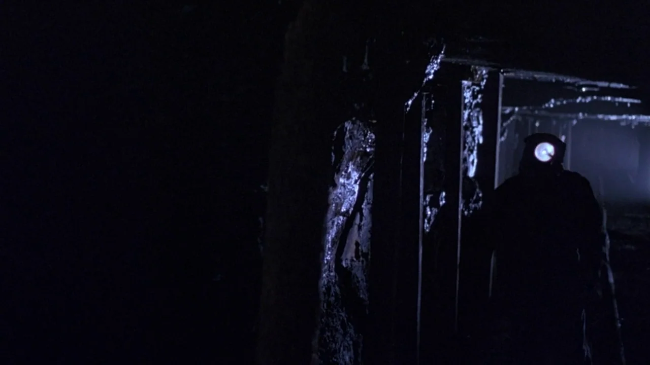 Matewan (1987) movie still: wide — A dark, narrow underground passage with damp, textured walls and visible structural supports. A single person…