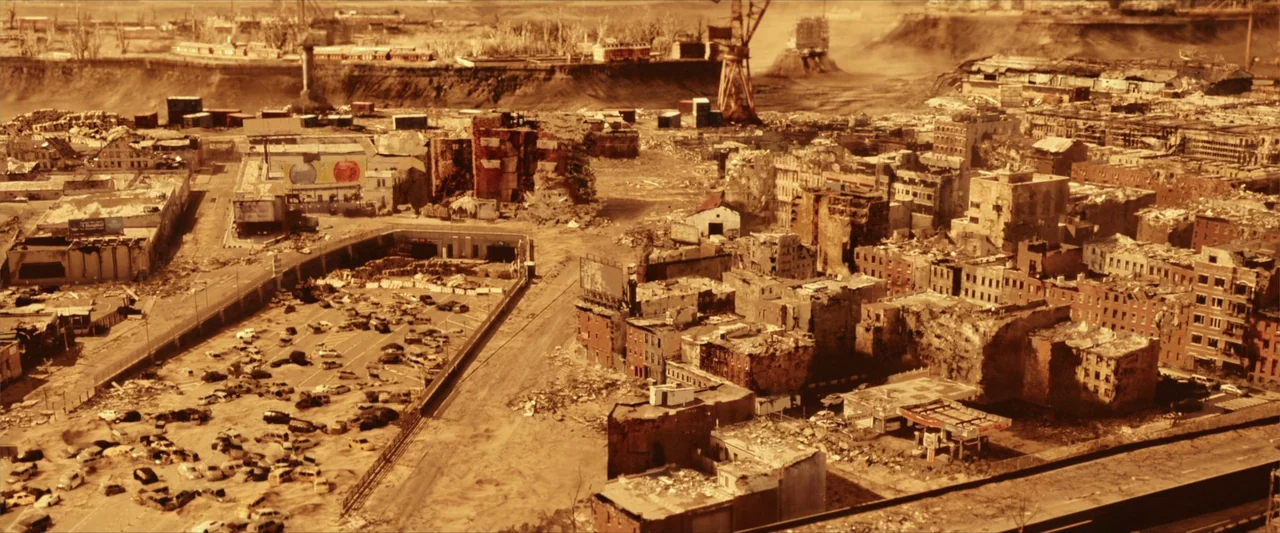Breathe (2011) movie still: establishing — A decimated cityscape features crumbling brick buildings, abandoned vehicles, and debris-filled streets.…