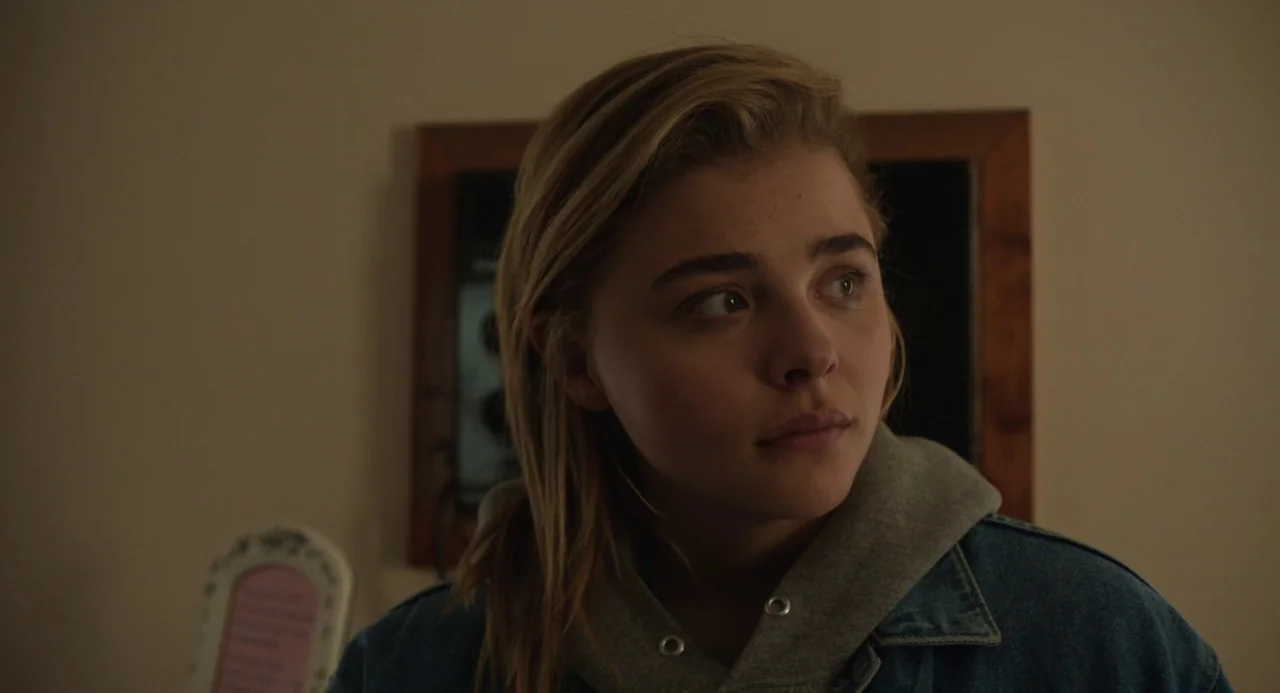 The Miseducation of Cameron Post (2018) movie still: closeup — A dimly lit room with plain walls features a wooden frame in the background. A woman…