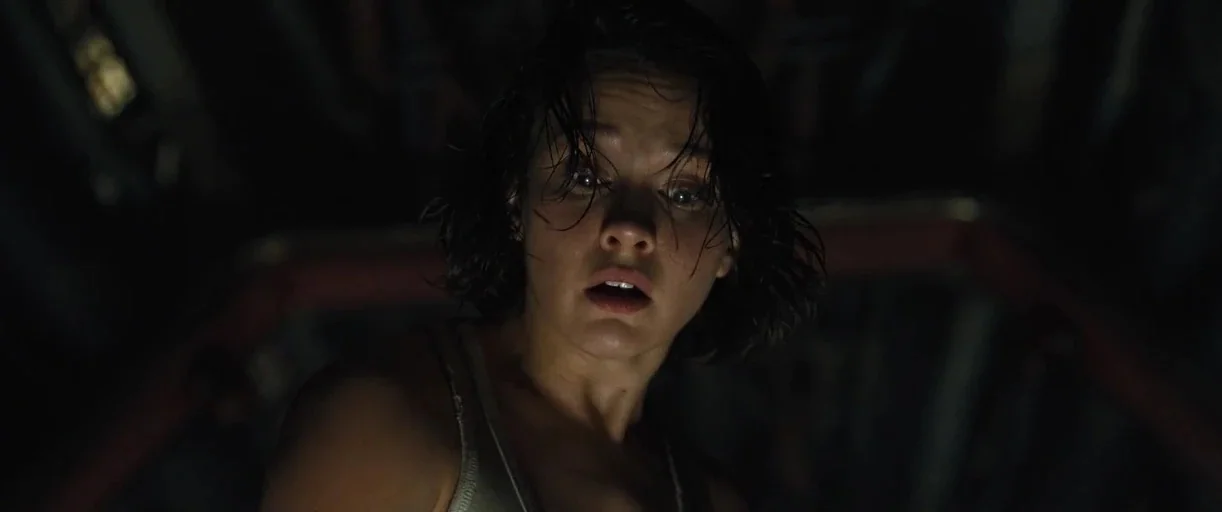 Alien: Romulus (2024) movie still: closeup — A dark, cramped interior with metallic textures and dim lighting. A young woman with damp hair looks…