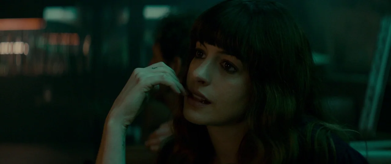 Colossal (2016) movie still: closeup — A dimly lit interior space with dark, indistinct surroundings and greenish ambient tones. A woman with dark…