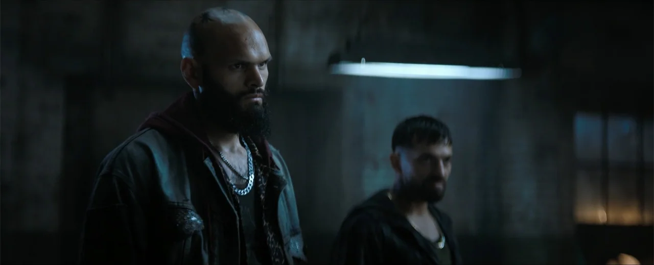 Venom: The Last Dance (2024) movie still: medium — A dark, textured industrial space features shadowed brick walls and dim atmospheric lighting. Two…