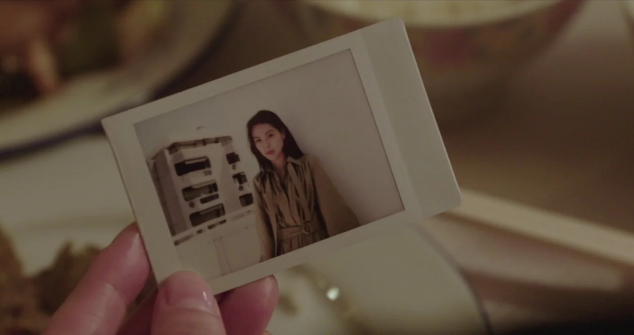 Claire’s Camera (2017) movie still: closeup — A close-up view of a person holding an instant polaroid photo. The photo depicts a young woman…