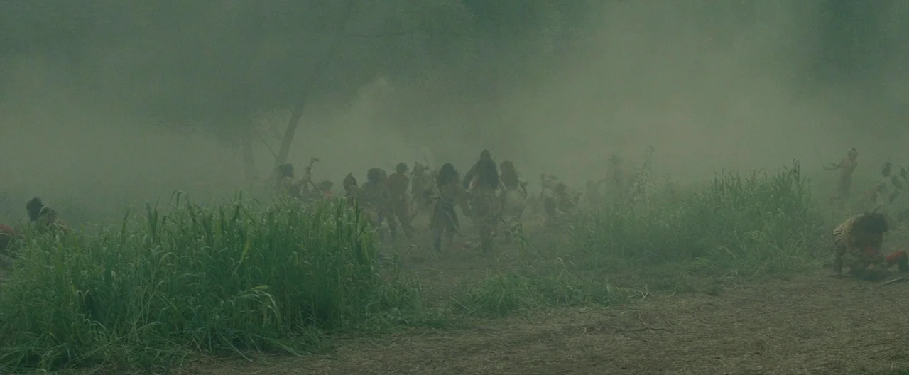 The Last of the Mohicans (1992) movie still: wide — A field filled with tall grass and thick, low-hanging smoke or fog. A large group of people are…