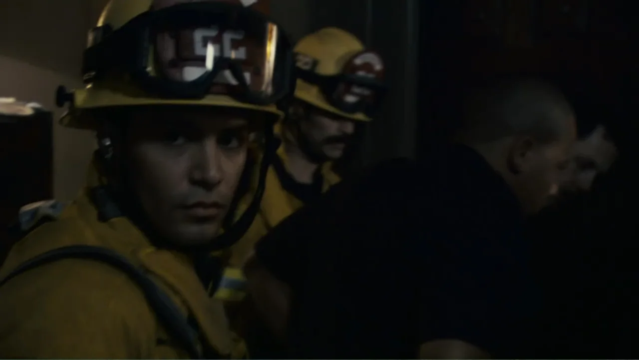 Quarantine (2008) movie still: medium — A dark indoor space contains multiple figures dressed in professional protective gear. A firefighter looks…