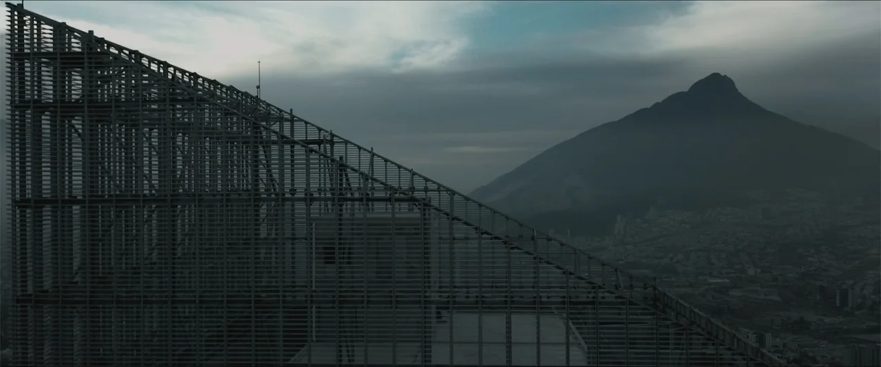 Los habitantes (2023) movie still: establishing — A high-angle view shows the metal framework of a modern building rooftop structure. A large…