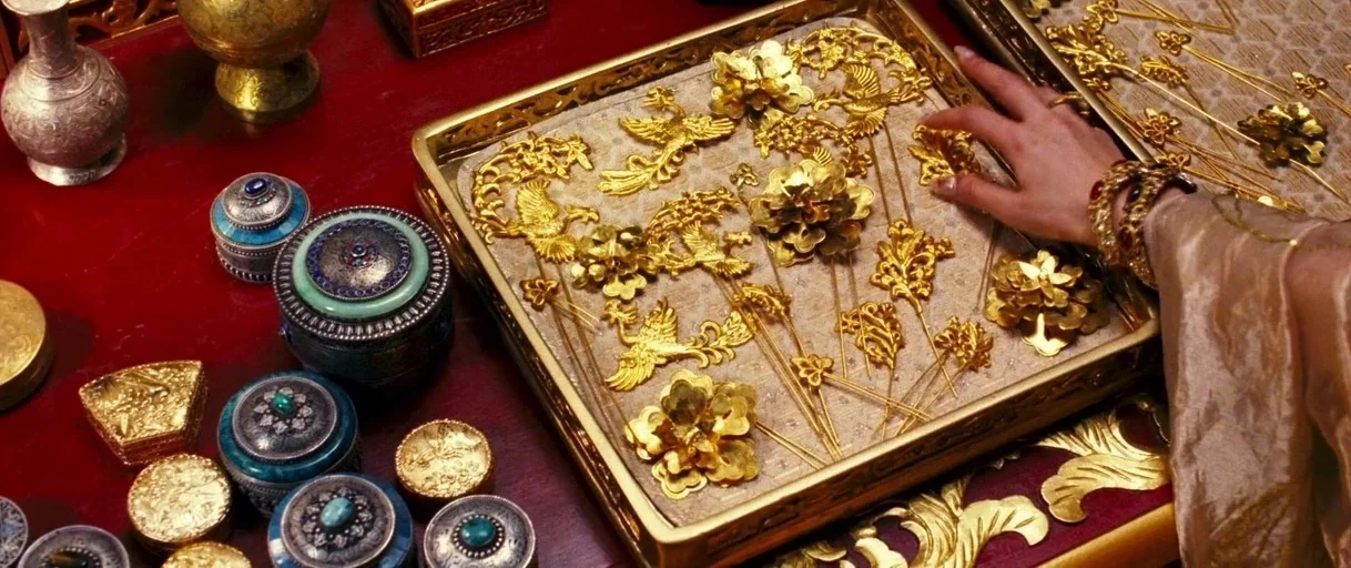 Curse of the Golden Flower (2006) movie still: closeup — A dark red table surface holds various silver containers with inlaid turquoise gemstones. A…