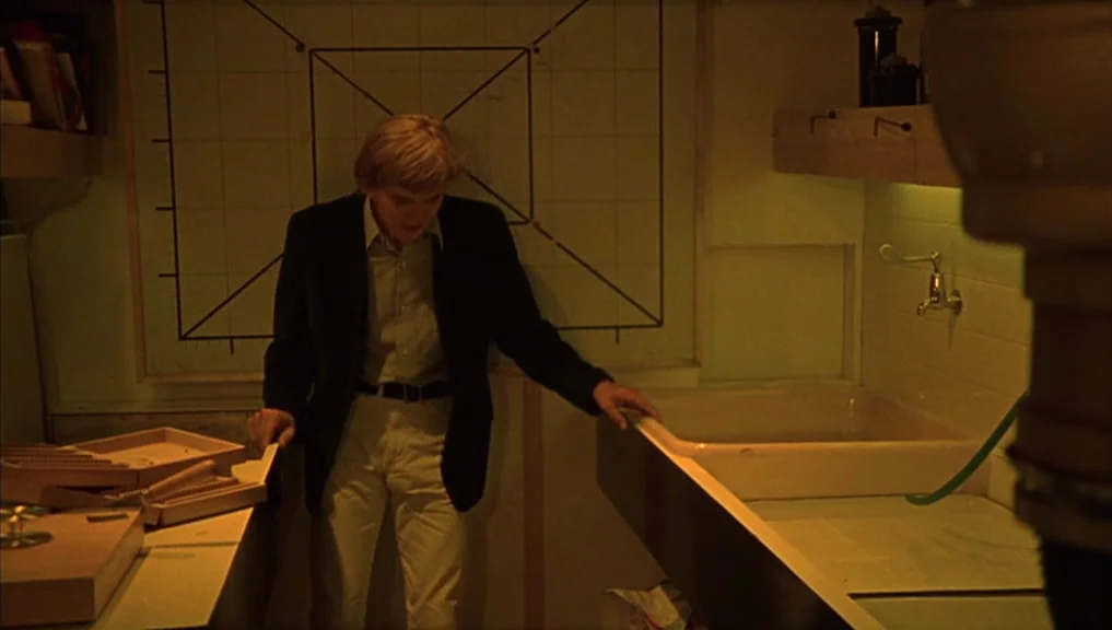 Blow-Up (1966) movie still: medium — A dimly lit industrial darkroom contains equipment and a large wall-mounted geometric grid chart. A young man…