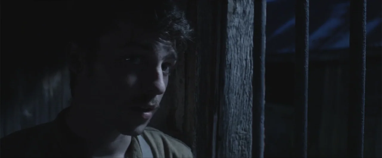 Behind the Line: Escape to Dunkirk (2020) movie still: closeup — A dimly lit, narrow prison cell features vertical metal bars and rough stone walls.…
