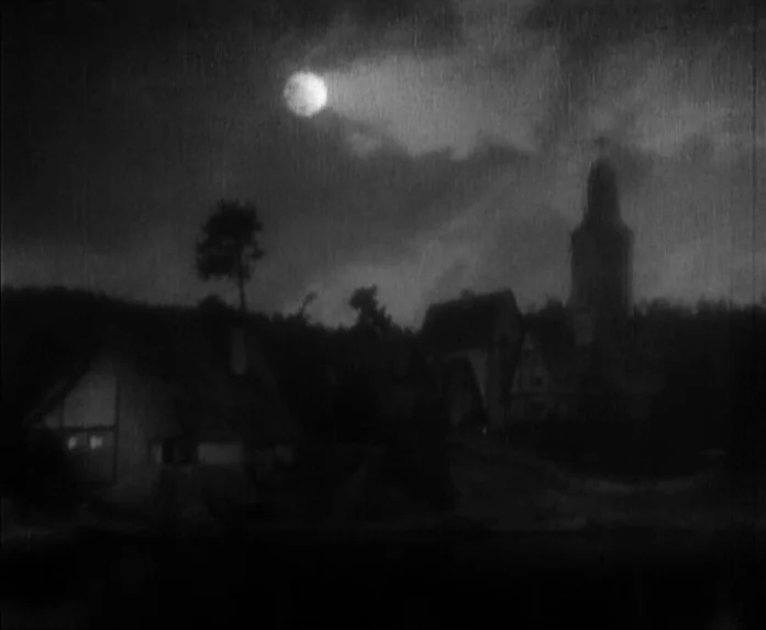 Sunrise (1927) movie still: establishing — A dark, rural village sits under a bright moon in a cloudy night sky. Silhouette shapes of houses and a…