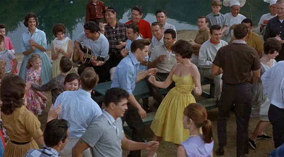 Kid Galahad (1962) movie still: wide — A group of young adults congregates near a shoreline for an outdoor social gathering. Elvis Presley dances…