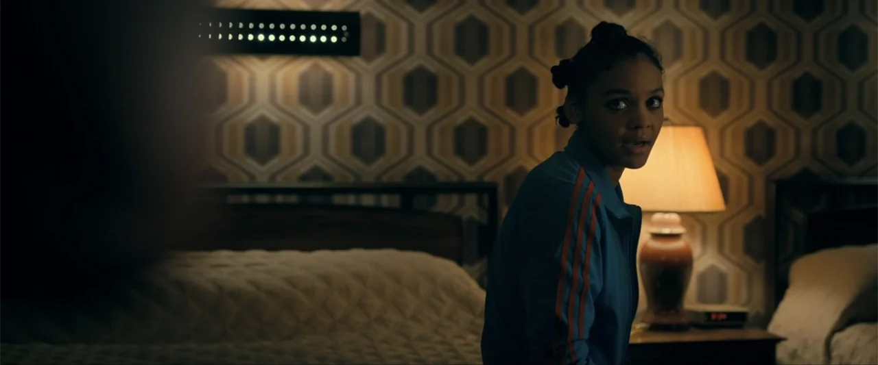 Madame Web (2024) movie still: medium — A dimly lit bedroom features patterned geometric wallpaper and beds with simple bedding. A young woman in a…