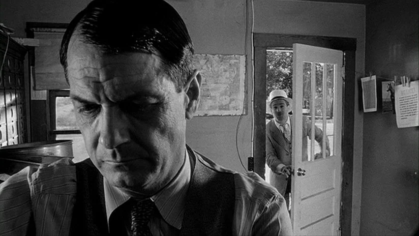 Paper Moon (1971) movie still: closeup — A small cluttered office with a map pinned to the wall. A man enters the doorway as another man stands in…
