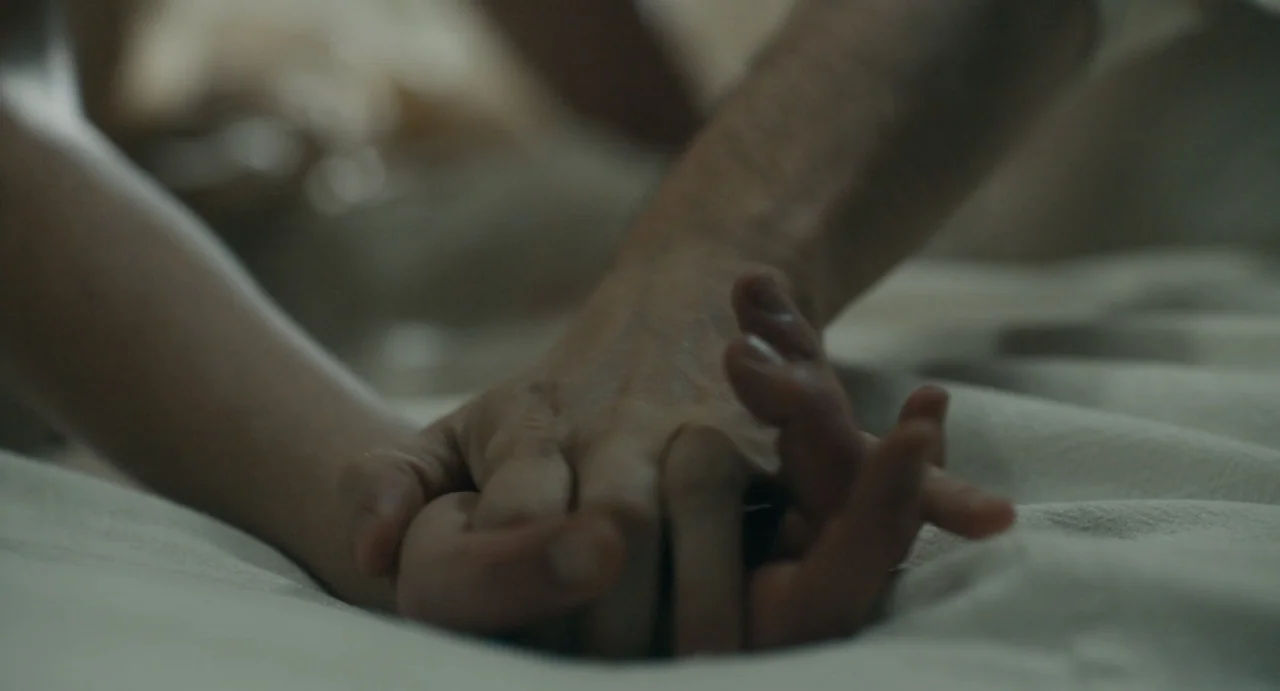 Catherine Called Birdy (2022) movie still: closeup — A close view shows two hands resting together on a textured white fabric surface. The hands are…