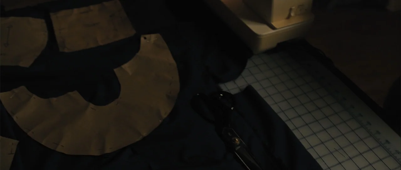 Carrie (2013) movie still: closeup — A dark workspace shows fabric patterns laid out on a cutting mat next to scissors. A sewing machine sits in the…
