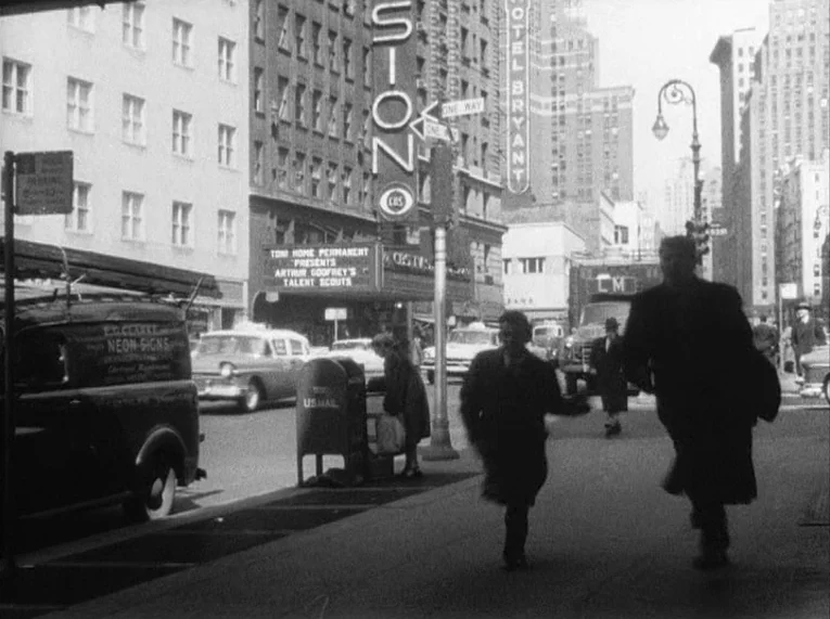 Shadows (1958) movie still: wide — A bustling 1950s New York city street features a theater marquee and vintage cars. Pedestrians move rapidly along…