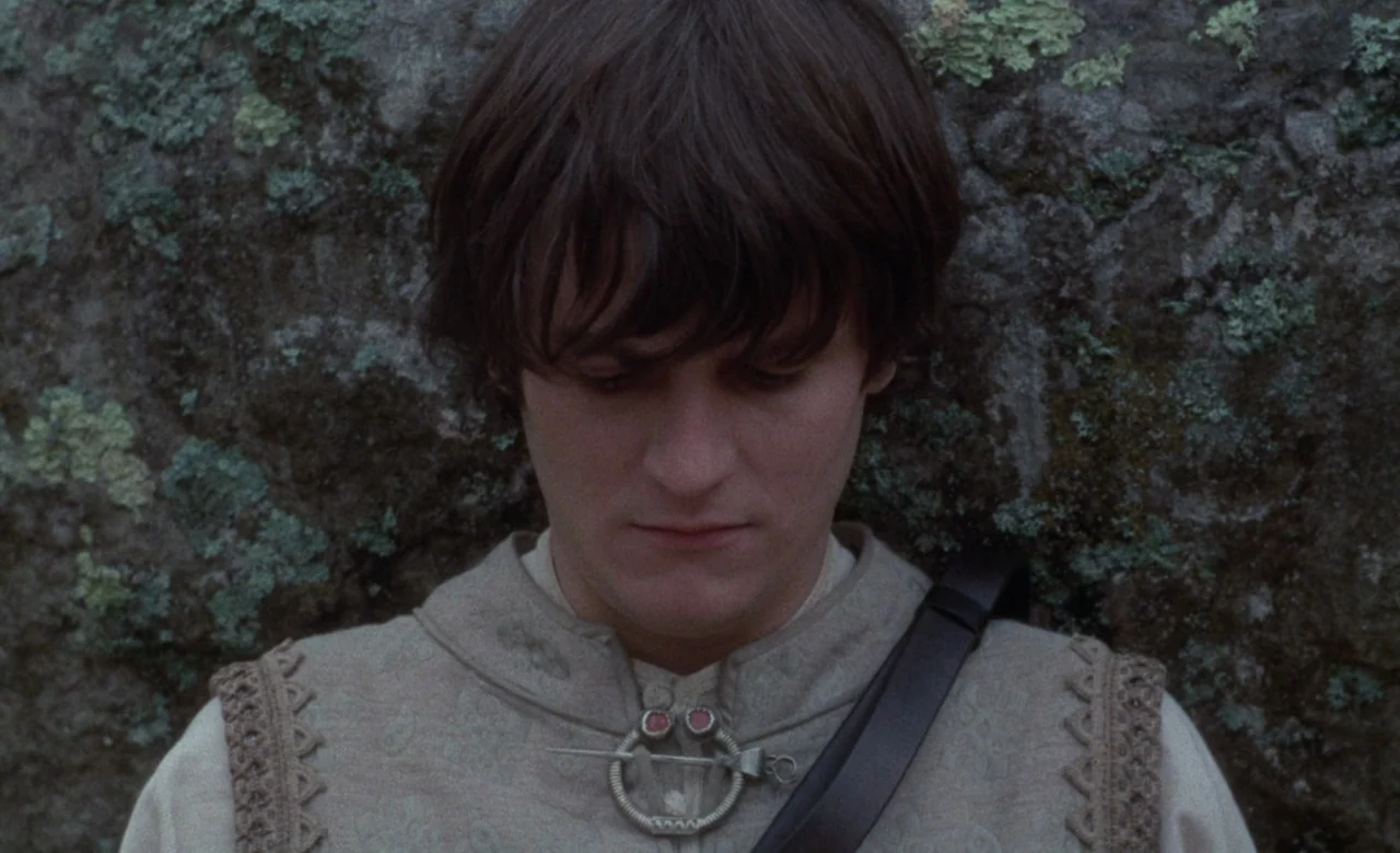 Blanche (1971) movie still: closeup — A man stands in front of a grey rock surface covered in green lichen. He is looking down while wearing a beige…