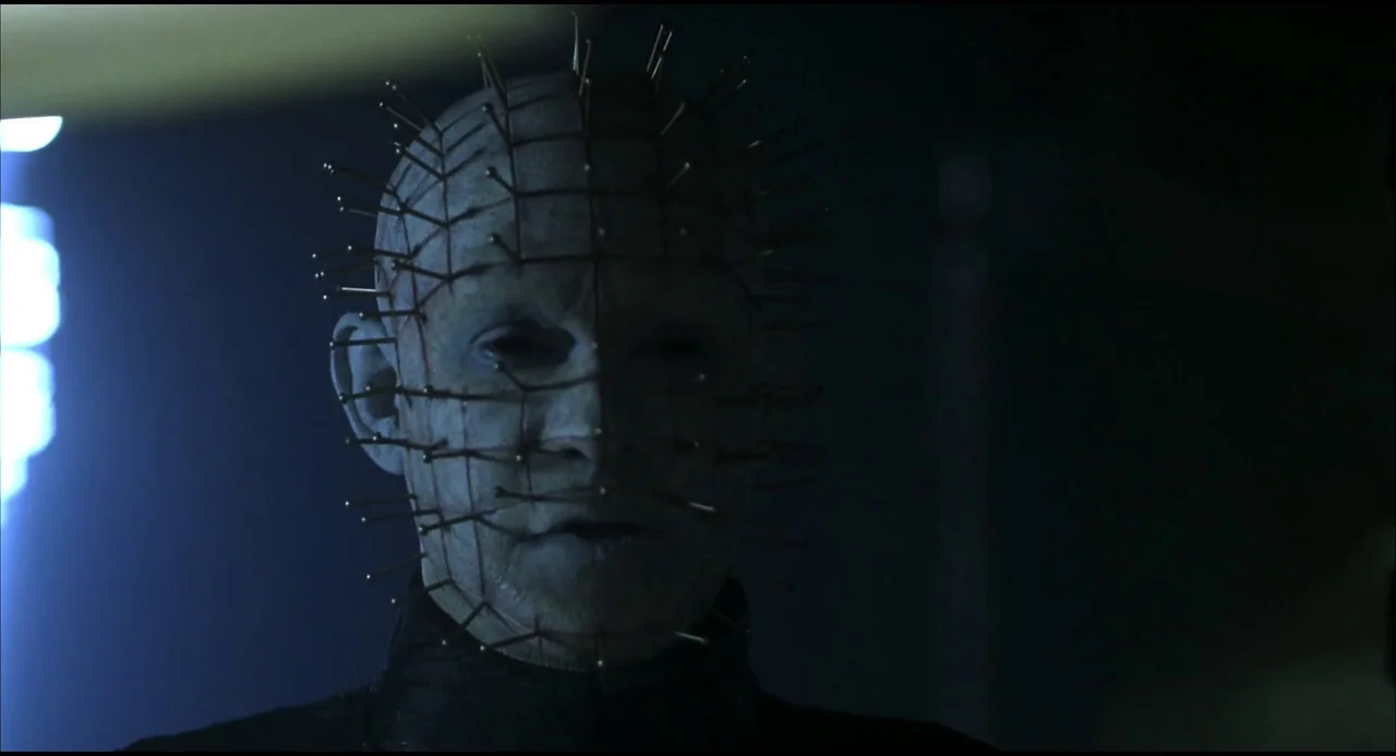 Hellraiser: Hellseeker (2002) movie still: closeup — A pale, bald figure covered in metal pins stands in a dark, indistinct environment. The…