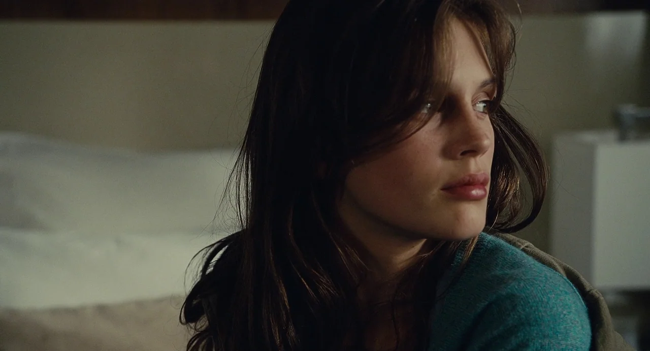 Young & Beautiful (2013) movie still: closeup — A hotel room interior featuring a bed with blurred white pillows in the background. A young woman…