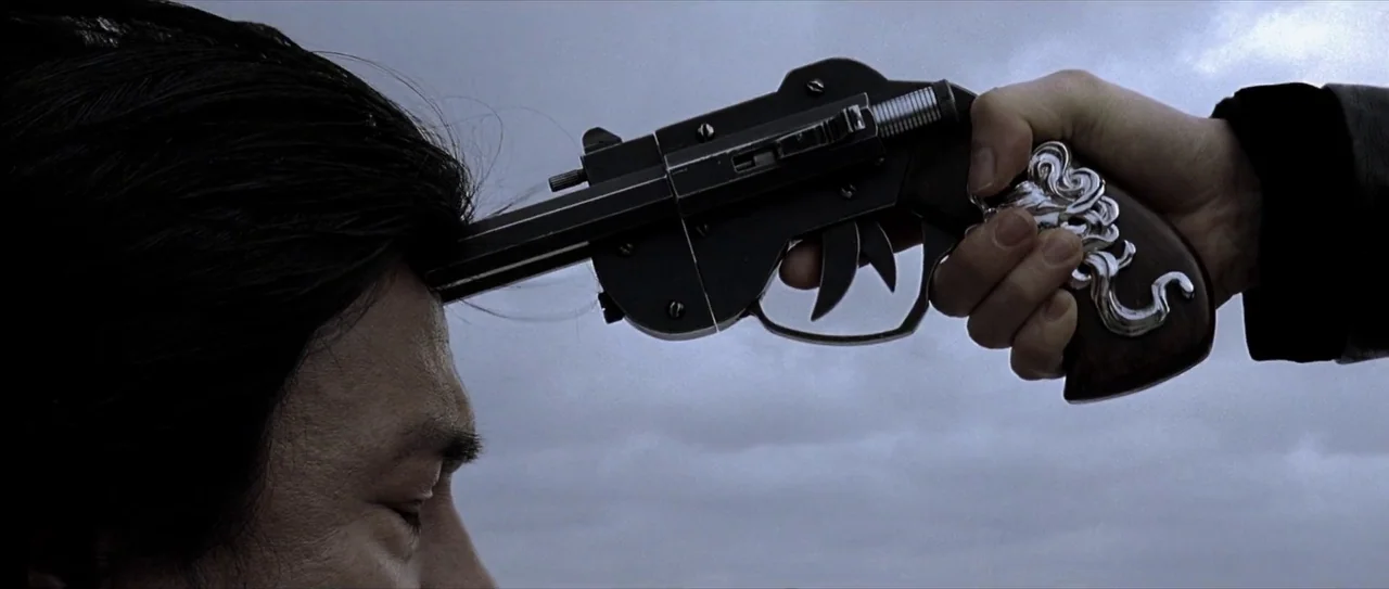 Lady Vengeance (2005) movie still: closeup — An overcast sky serves as a uniform background for a close-up interaction. A hand holds a decorative…