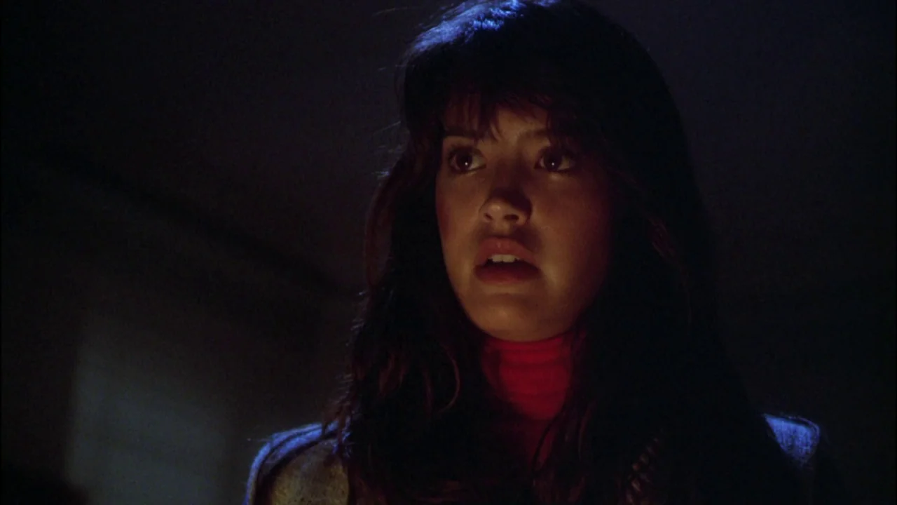 Gremlins (1984) movie still: closeup — A woman stands in a dark environment with indistinct architectural features behind her. She looks toward the…