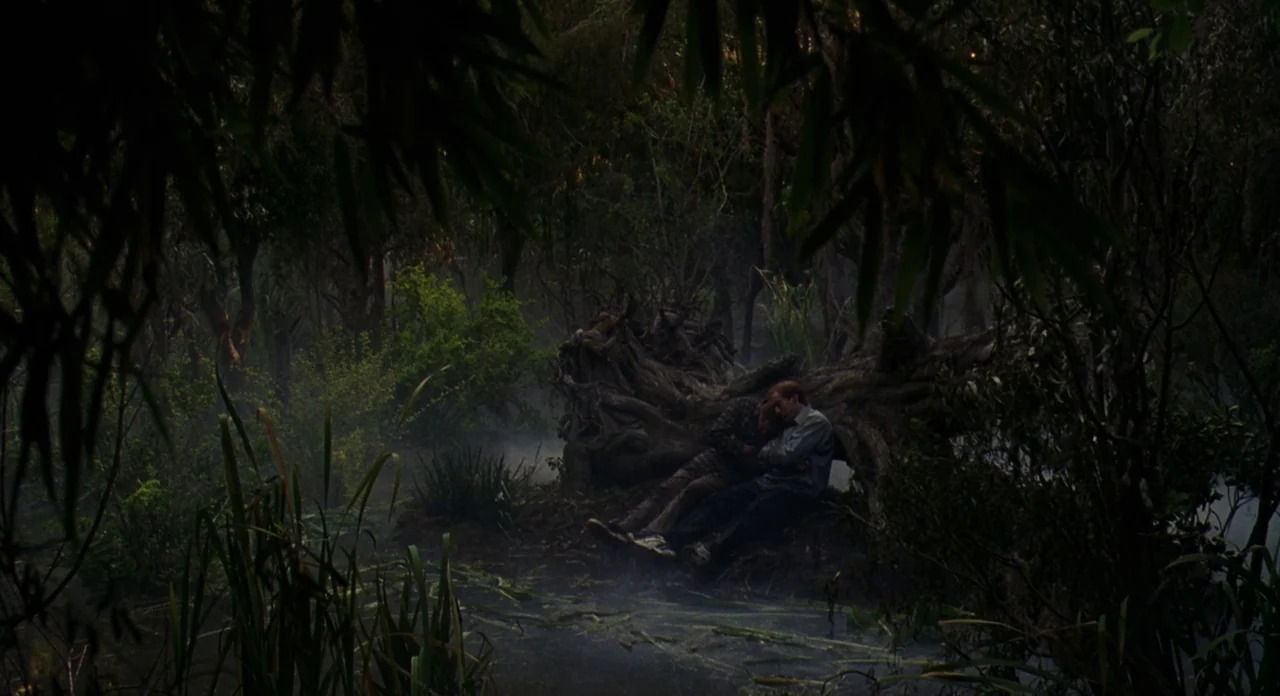Adaptation (2002) movie still: wide — A dense, dark swamp is filled with low-hanging fog and tall, dense vegetation. Two men are huddled together…