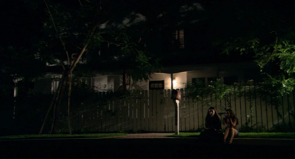 Me and You and Everyone We Know (2005) movie still: wide — A dark residential street features a white picket fence and a wooden house. Two young…