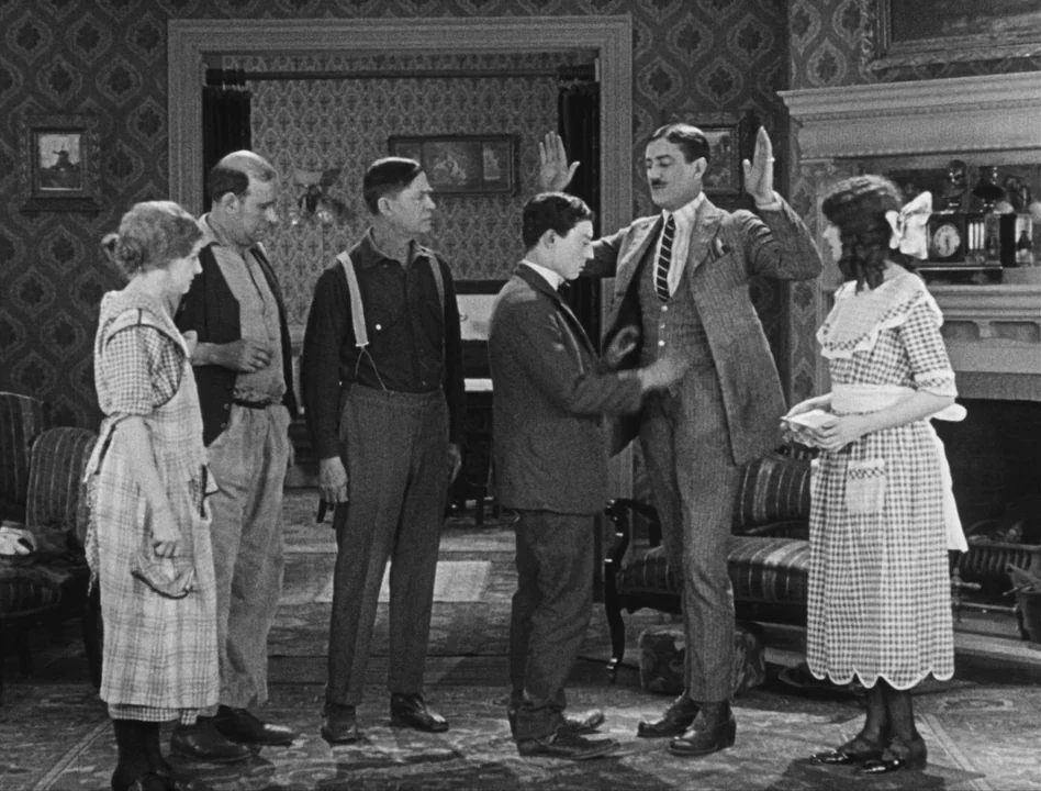 Sherlock Jr. (1924) movie still: fullbody — A 1920s living room features ornate patterned wallpaper, a fireplace mantel, and period furniture. A man…