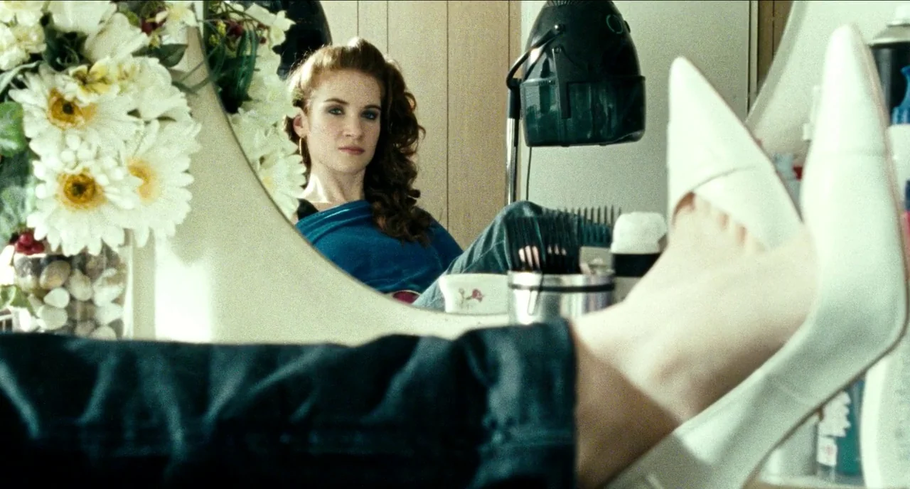 Bronson (2008) movie still: medium — A beauty salon vanity holds a hair dryer and floral arrangement against a mirror. A woman rests her feet in…