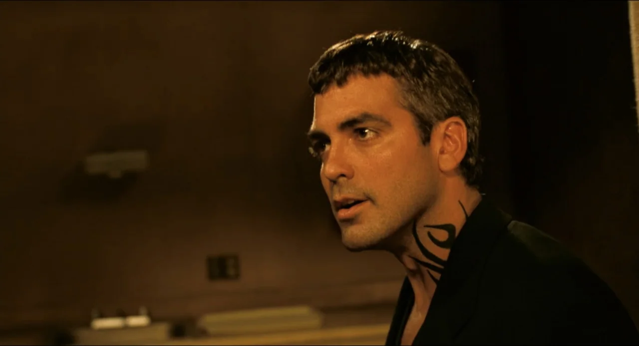 From Dusk Till Dawn (1996) movie still: closeup — A dimly lit interior space contains a man standing against a dark wall. A man with a neck tattoo…