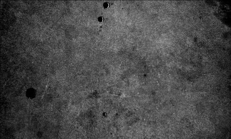 Pi (1998) movie still: establishing — A dark, textured background exhibits heavy grain and several circular light artifacts. The surface appears to…